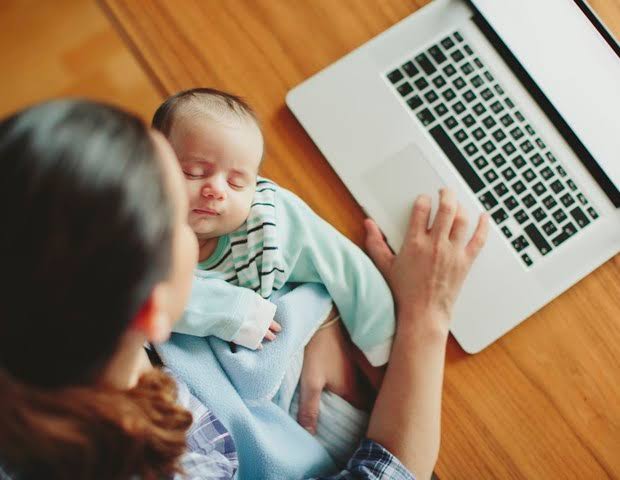 Progenitor com um bebé junto de um computador, representando a necessidade de conciliar trabalho e cuidado